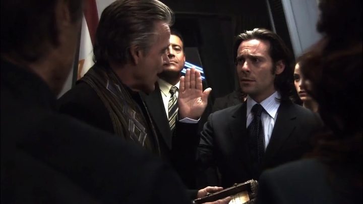 Gaius Baltar raises his hand as he is sworn in as President in the Battlestar Galactica episode "Lay Down Your Burdens, Part 2"
